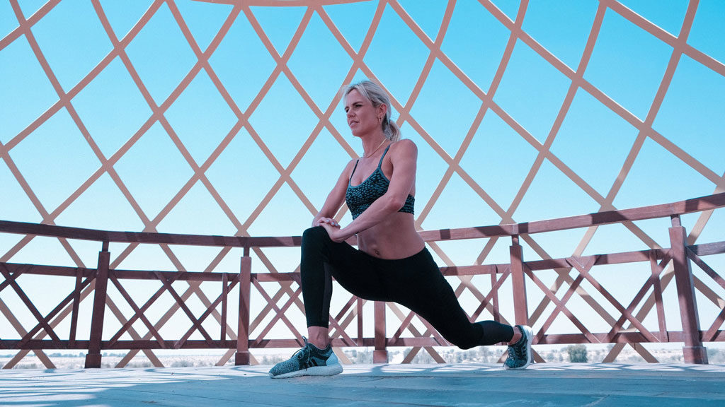 Woman in green sports bra and black leggings doing a lunge