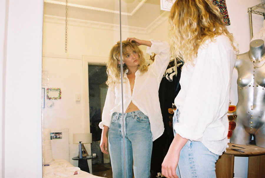 Claudia looks in the mirror wearing a white blouse and blue jeans