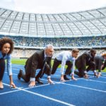 Side view photo of confident multi ethnic business people lined up getting ready for race on modern sport track. Stadium as a background