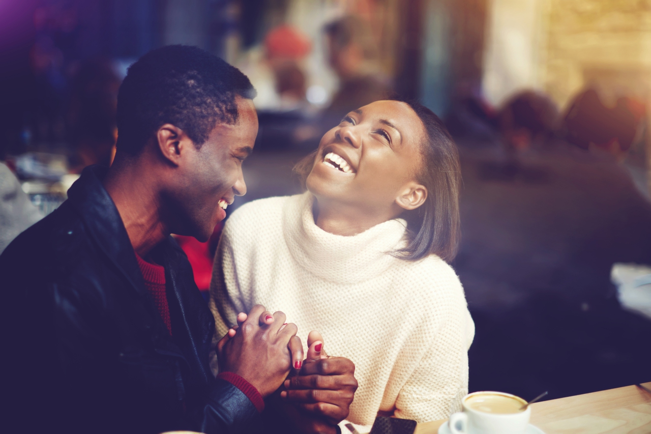 Young happy man and woman laughing together while sitting in modern restaurant during coffee break, cheerful couple in love with smiles on faces enjoying rest and good day while relaxing in bar