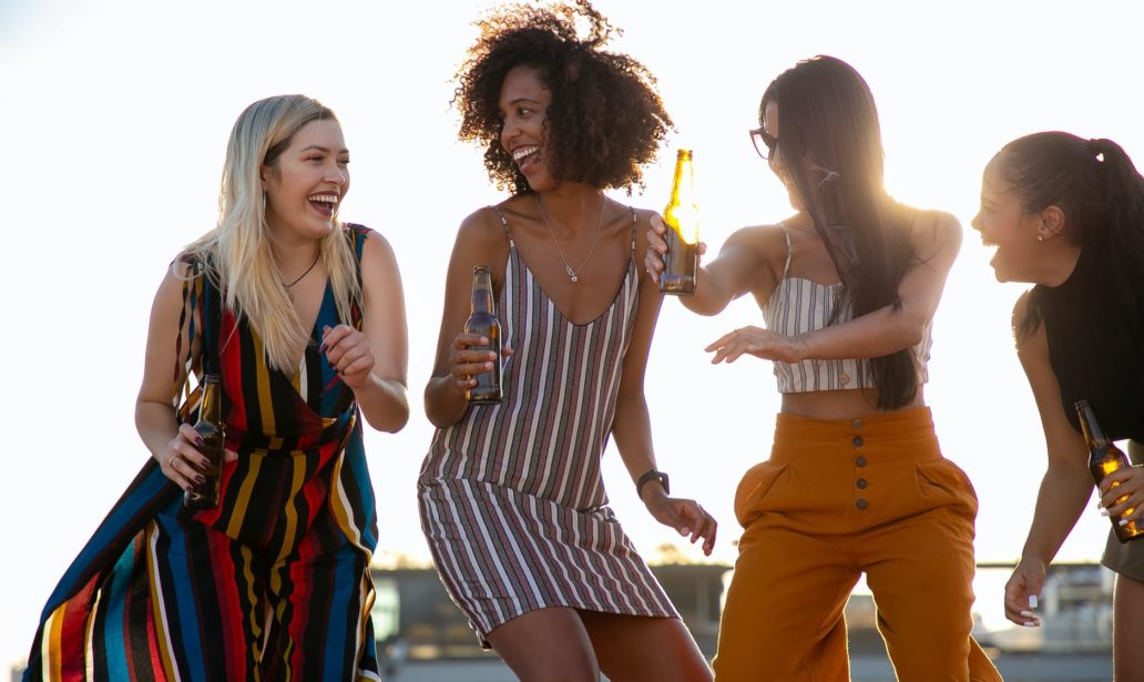 laughing young diverse girlfriends dancing and drinking beer during event