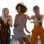 laughing young diverse girlfriends dancing and drinking beer during event