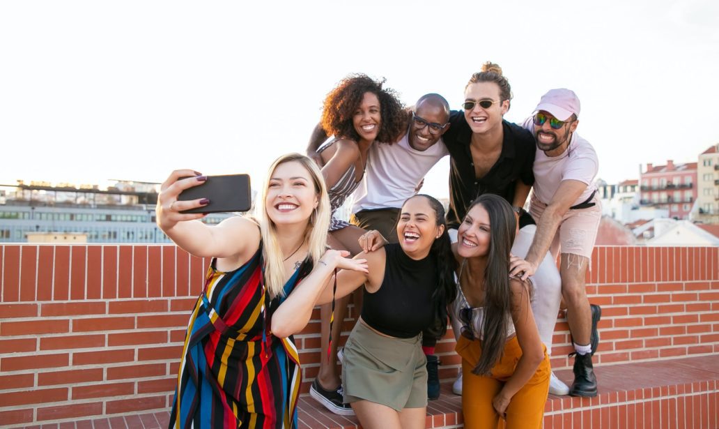 excited young diverse men and women taking selfie on rooftop