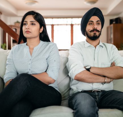 offended young indian couple sitting on sofa