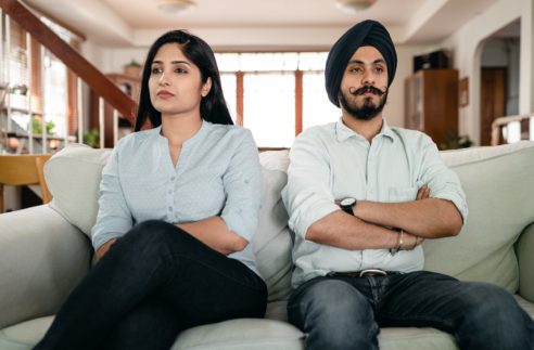 offended young indian couple sitting on sofa
