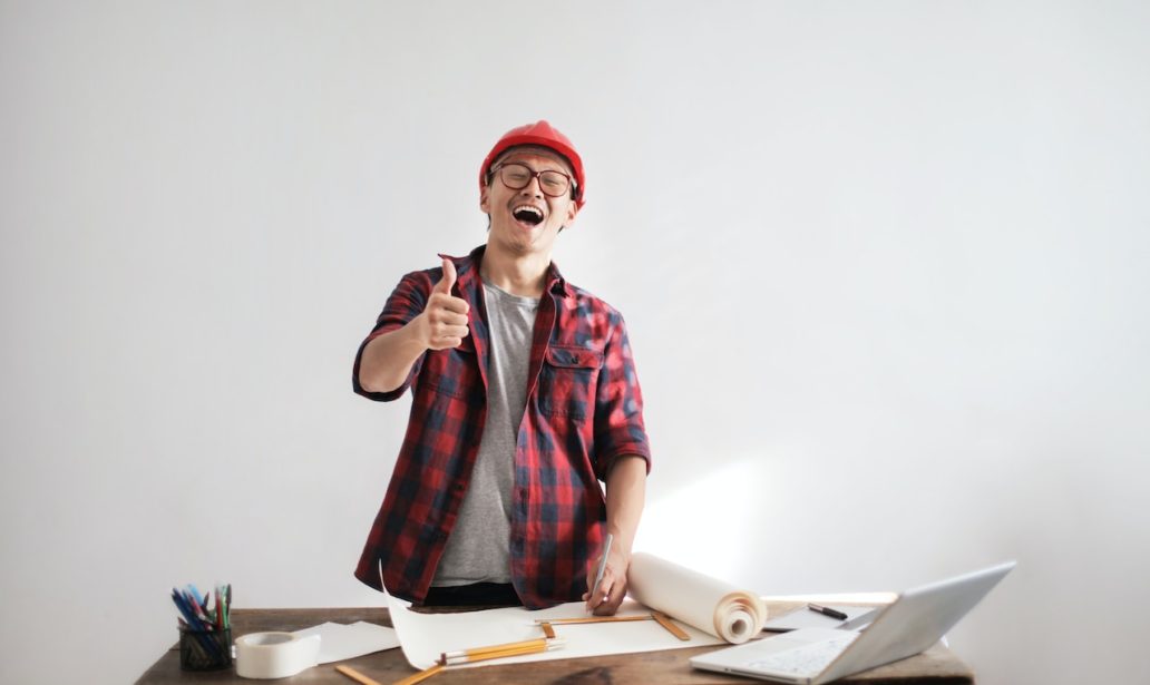 Laughing male constructor showing thumb up at working desk