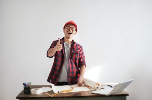 Laughing male constructor showing thumb up at working desk