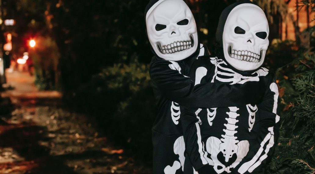 Unrecognizable children in skeleton costumes hugging on street