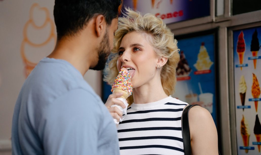 woman with tousled hair licking an ice cream and looking man's eyes
