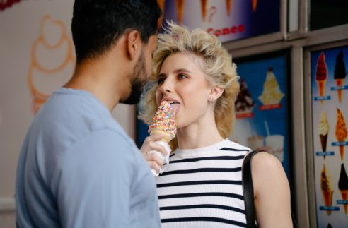 woman with tousled hair licking an ice cream and looking man's eyes