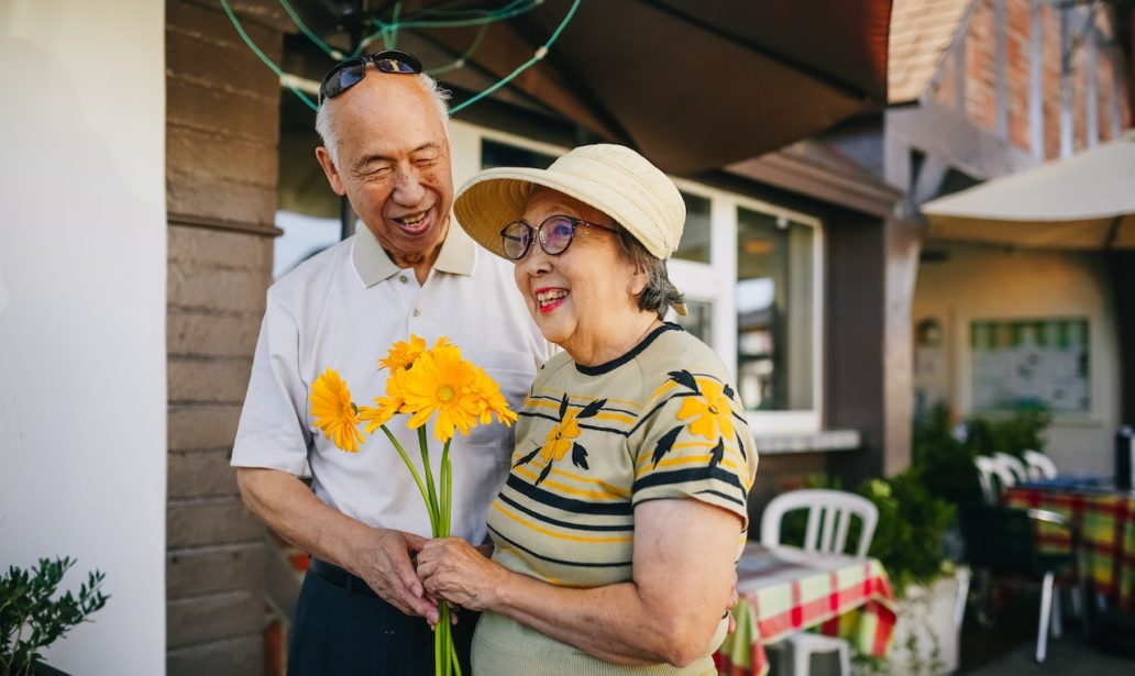 Elderly couple holding bouquet of flowers while holding hands