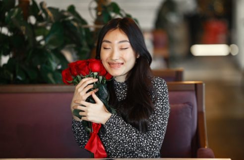 portrait of a girl with red roses sitting on a brown bench indoors