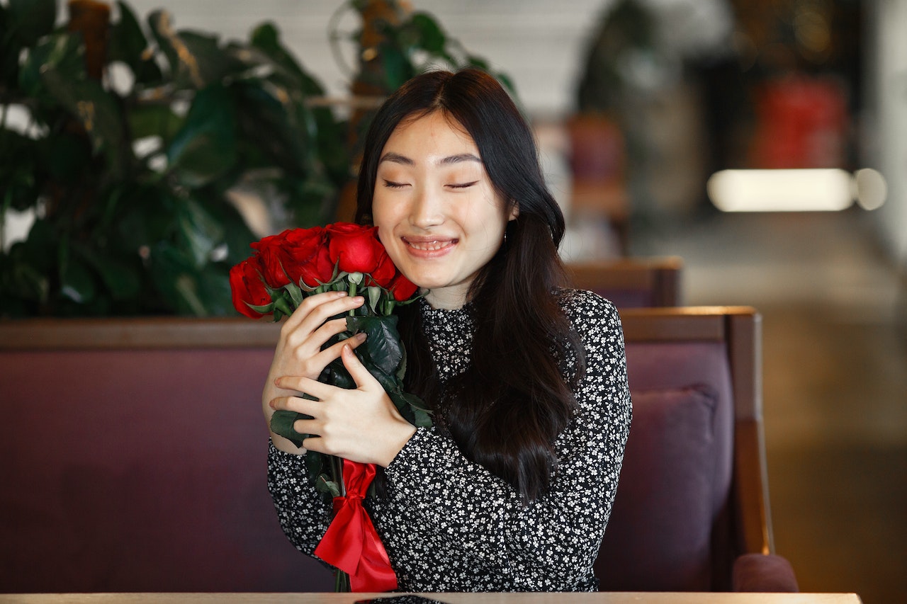 portrait of a girl with red roses sitting on a brown bench indoors