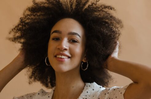 cheerful young black lady touching afro hair and smiling