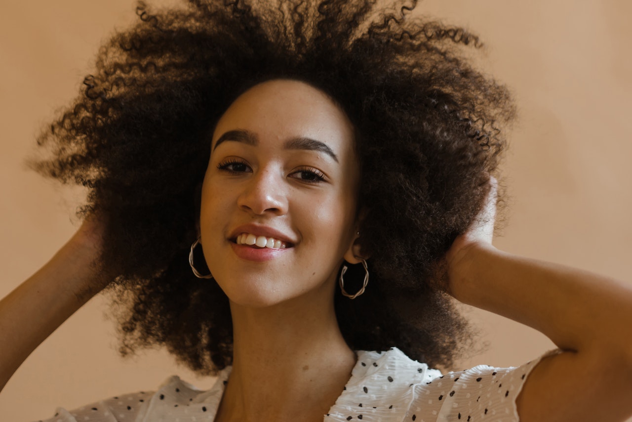 cheerful young black lady touching afro hair and smiling