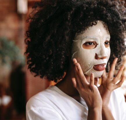 calm black lady applying sheet mask for treatment procedure