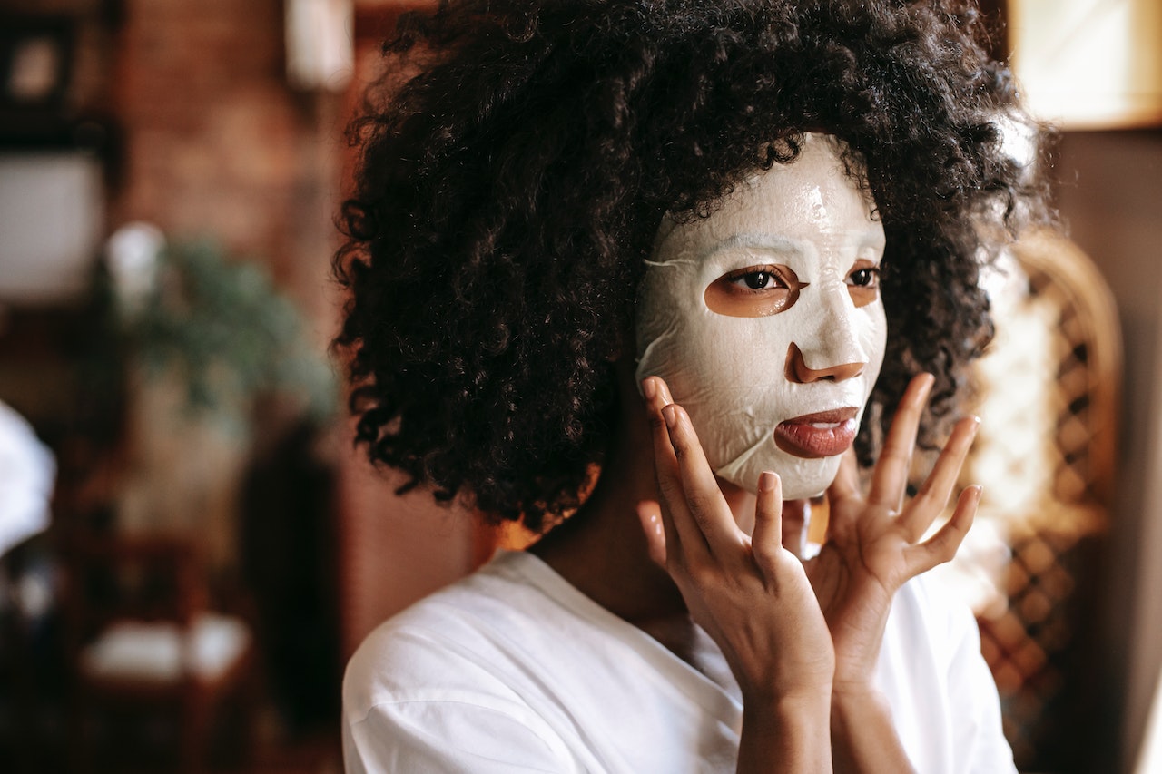 calm black lady applying sheet mask for treatment procedure