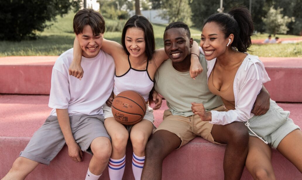 happy multiracial friends embracing on bench after playing basketball