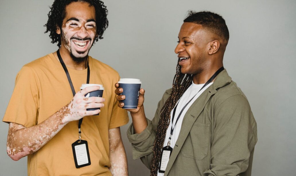 happy african american colleagues standing with cups of coffee and laughing