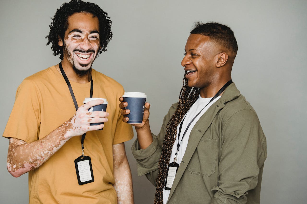 happy african american colleagues standing with cups of coffee and laughing