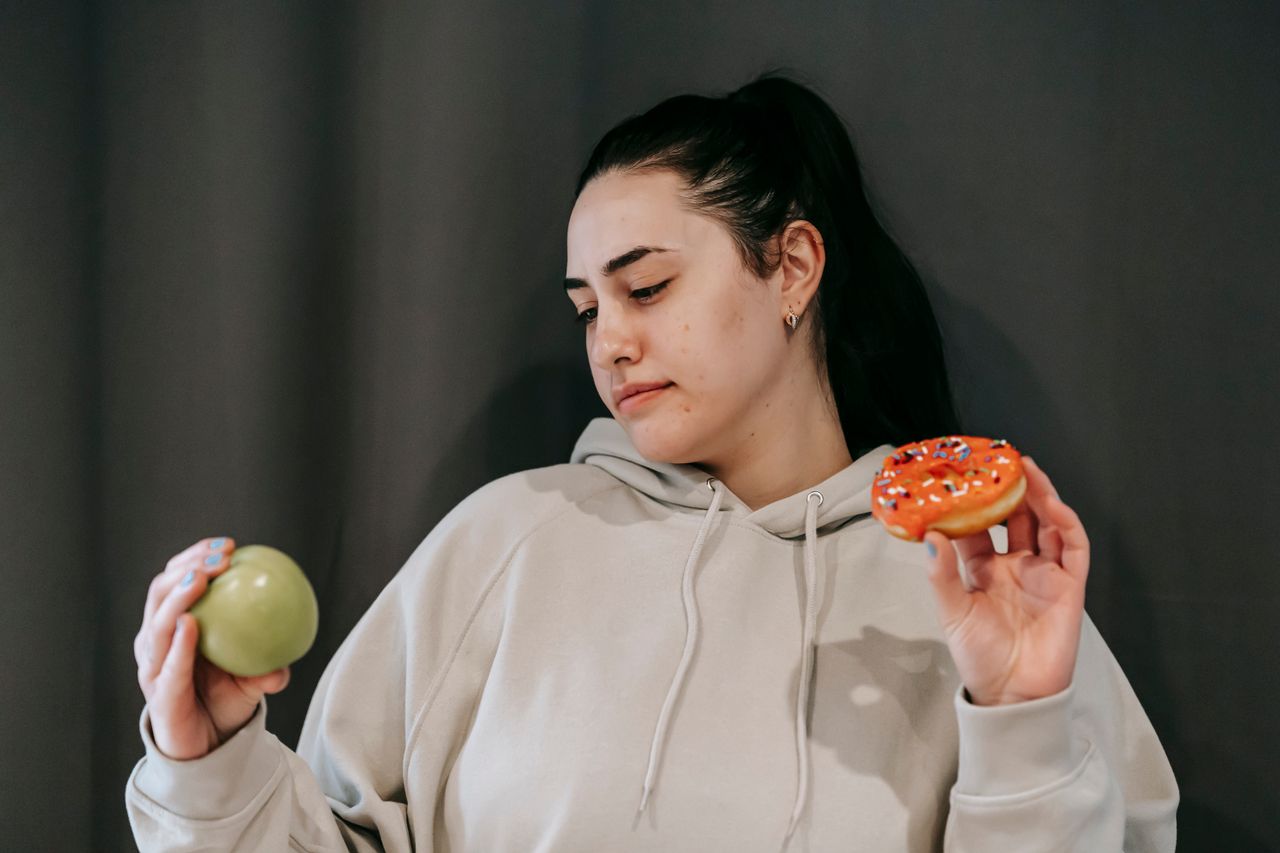 thoughtul woman choosing between green apple and donut