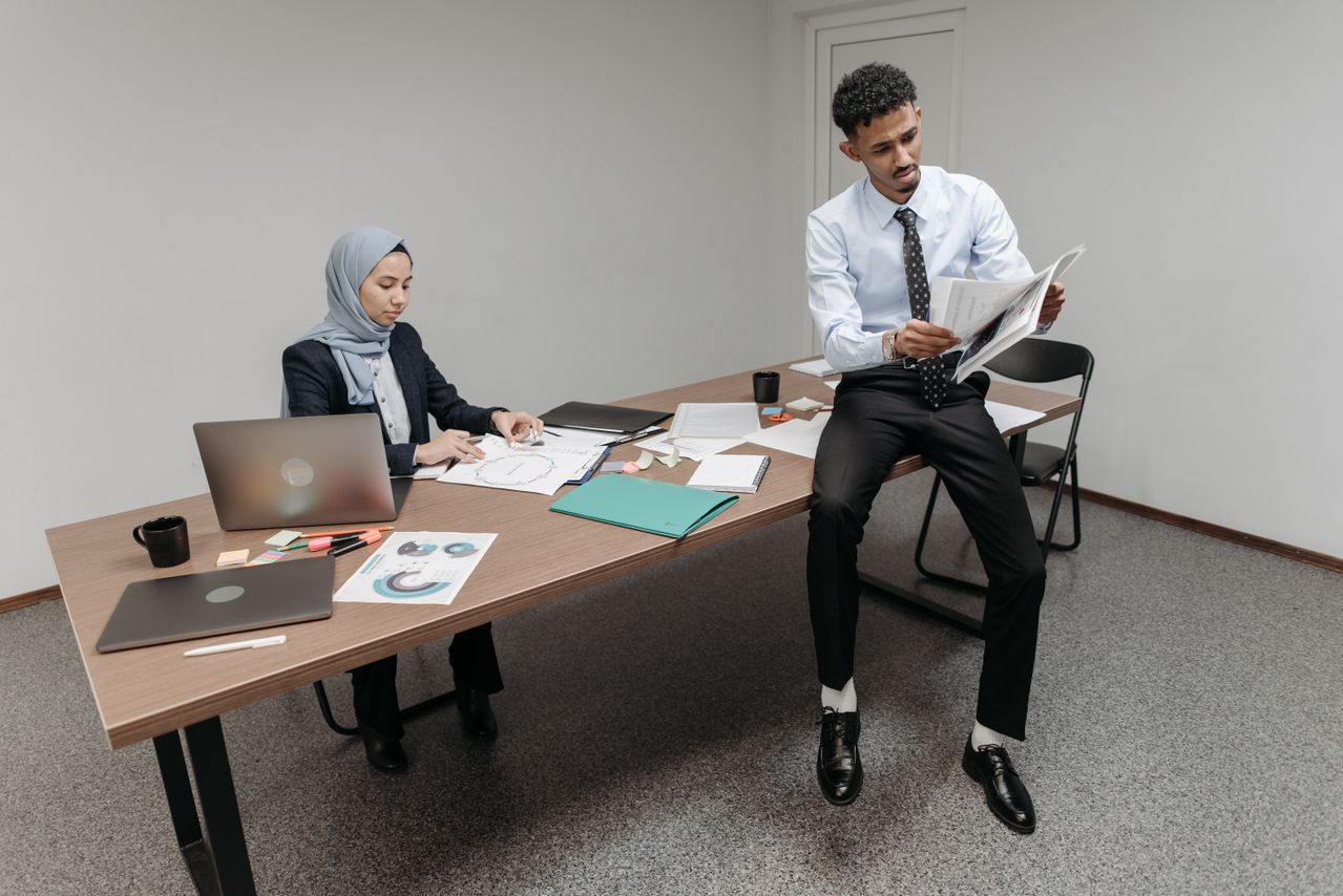 Two colleagues working on documents and laptops in a modern office setting.